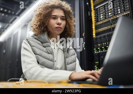 Techniker mit lockigem Haar, der im Serverraum am Laptop arbeitet Stockfoto