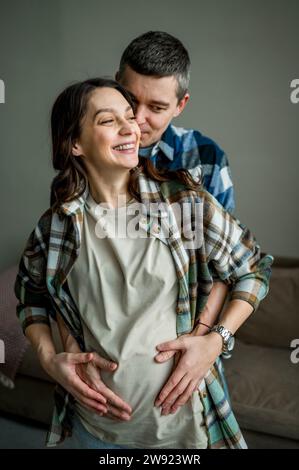 Liebevoller Mann, der zu Hause die Hände einer schwangeren Frau auf dem Magen hält Stockfoto