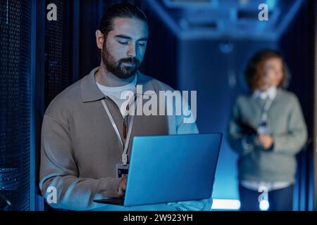 Junger IT-Ingenieur mit Laptop und Kollegen im Hintergrund Stockfoto