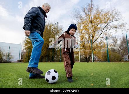 Senior Mann und Enkel spielen mit Ball auf dem Fußballfeld Stockfoto