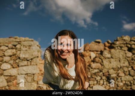 Lächelnde Frau, die sich auf den Ellenbogen vor einer Steinmauer stützt Stockfoto