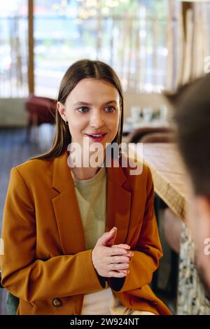 Junge Frau in Blazer, die mit einem Kollegen im Restaurant spricht Stockfoto
