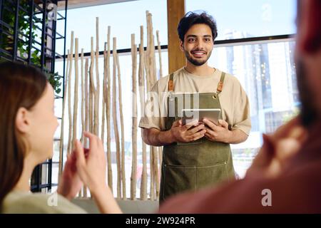 Lächelnder Kellner, der im Restaurant Essensbestellungen von Gästen entgegennimmt Stockfoto