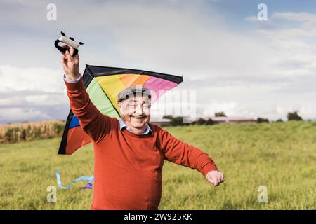 Glücklicher Senior-Mann, der auf dem Feld einen mehrfarbigen Drachen fliegt Stockfoto