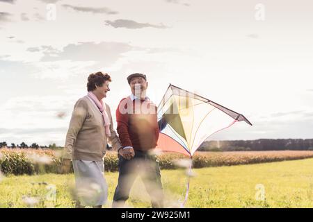 Glückliches Seniorenpaar, das Hände hält und mit Drachen auf dem Feld läuft Stockfoto