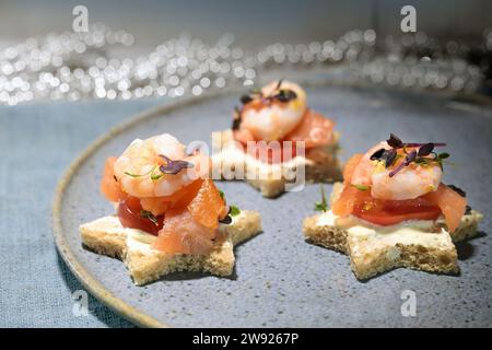 Canape Sandwiches in Sternform mit Garnelen und Lachs auf blauem Teller, Snack für eine festliche Feiertagsfeier wie Weihnachten oder Silvester, Cop Stockfoto