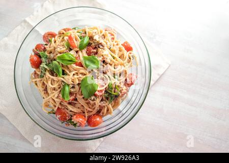 Kalter Spaghetti-Salat mit Tomaten, Rucola, Mozzarella, Oliven und einem cremigen Dressing mit Basilikumgarnitur in einer Glasschale auf einem weiß bemalten Tisch, oben Stockfoto