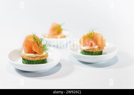 Kanapees als Party Fingerfood für das kalte Buffet aus Gurke, Crackern, Frischkäse, Räucherlachs und Dill auf kleinen weißen Tellern, Kopierraum, Stockfoto