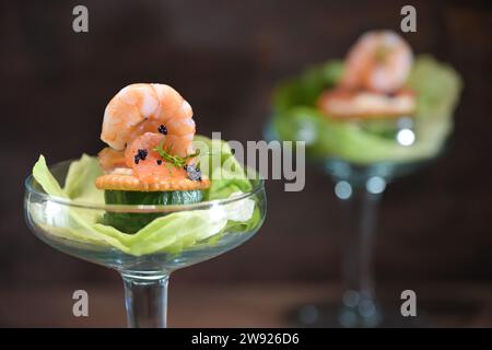 Vorspeise oder Party-Snack mit Lachs, Garnelen und Kaviar auf Salat, serviert in einem Cocktailglas vor dunklem Hintergrund für Feiertage wie Weihnachten und Weihnachten Stockfoto