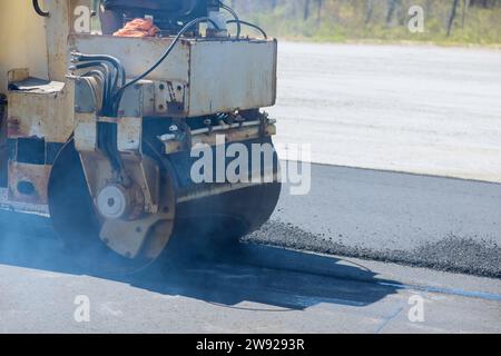 Beim Bau neuer Straßen wird eine Asphaltwalzenwalze vom Arbeiter verwendet Stockfoto