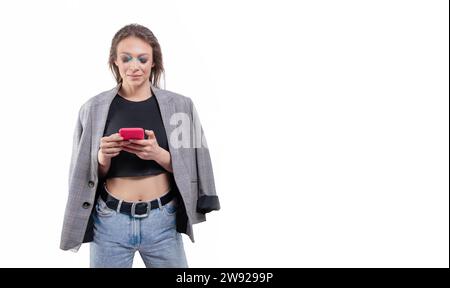 Porträt eines schönen Mädchens in einer Jacke mit einem Handy in der Hand. Weißer Hintergrund. Gemischte Medien Stockfoto