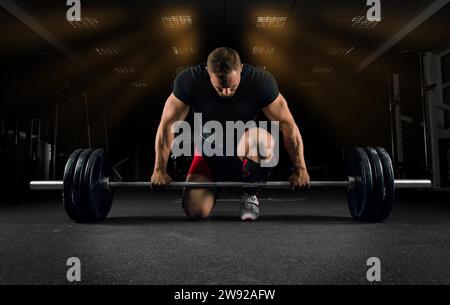 Der Athlet steht auf seinem Knie und in der Nähe der Bar im Fitnessstudio und bereitet sich auf einen Deadlift vor Stockfoto