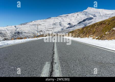 Leere Straße, die in Richtung schneebedeckter Berge unter einem klaren blauen Himmel führt Stockfoto