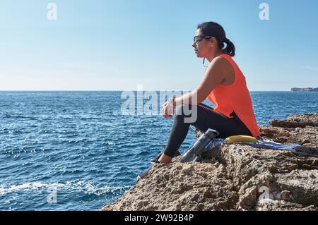 Lateinische Frau, mittleren Alters, ruht sich aus, gewinnt wieder an Kraft, isst, Trinkwasser, nach einem Fitnessraum, Kalorien verbrennen, fit halten, draußen beim Stockfoto