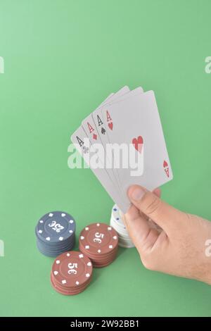Vier Asse fächern sich in einer Hand über gestapelten Pokerchips auf einer grünen Oberfläche, Pokerkarten und Chips auf Stockfoto