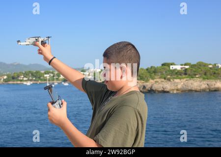 Porträt glücklicher Teenager Junge, Vorbereitung und Fertigstellung von Flugdetails für Drohnenflug, Mittelmeer Hintergrund an einem sonnigen Tag, Technologiekonzept Stockfoto