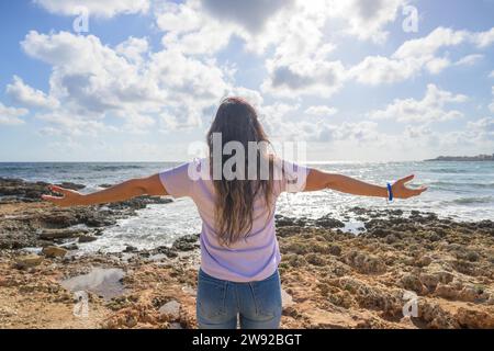 Frau mittleren Alters, die ihre Arme ausstreckt und frische Luft an der Mittelmeerküste vor der Sonne atmet Stockfoto