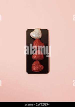 Rot leuchtende Herzen auf dem Smartphone-Bildschirm auf pastellrosa Hintergrund. Valentinstag-Konzept und Online-Dating. Stockfoto