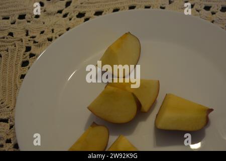 Schöne Scheiben geschnittener roter Apfel werden zufällig auf einer großen weißen Glasplatte auf dem Küchentisch angeordnet. Stockfoto