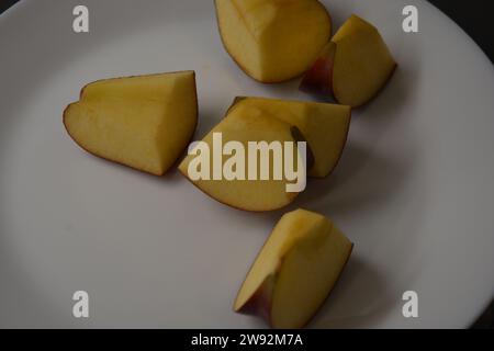 Schöne Scheiben geschnittener roter Apfel werden zufällig auf einer großen weißen Glasplatte auf dem Küchentisch angeordnet. Stockfoto