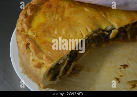 Ein übrig gebliebener hausgemachter Kuchen mit einer dünnen Teig- und Gemüsefüllung, bestehend aus Kohl, Pilzstücken und Zwiebeln, steht in einer stilvollen Küche. Stockfoto