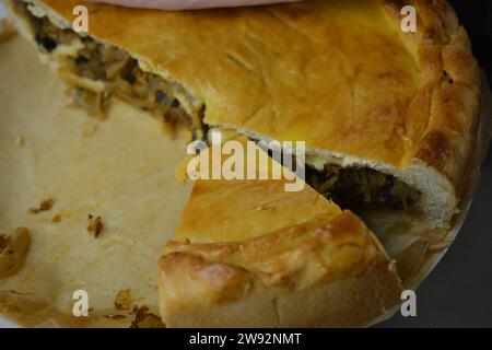 Ein übrig gebliebener hausgemachter Kuchen mit einer dünnen Teig- und Gemüsefüllung, bestehend aus Kohl, Pilzstücken und Zwiebeln, steht in einer stilvollen Küche. Stockfoto