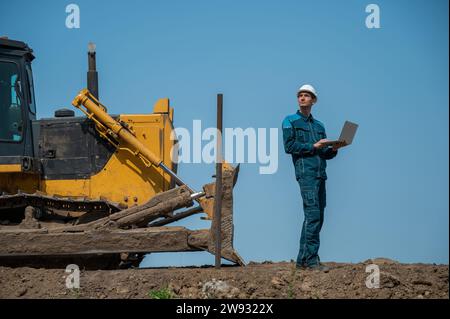 Weißer Baumeister im Schutzhelm, der auf der Baustelle einen Laptop hält. Stockfoto