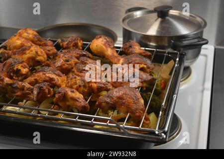 Hühnerstücke auf einem Metallgitter mit einem Backblech Gemüse wie Kartoffeln, Zucchini, Paprika, Zwiebeln, Brokkoli Stockfoto