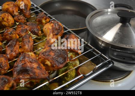 Hühnerstücke auf einem Metallgitter mit einem Backblech Gemüse wie Kartoffeln, Zucchini, Paprika, Zwiebeln, Brokkoli Stockfoto