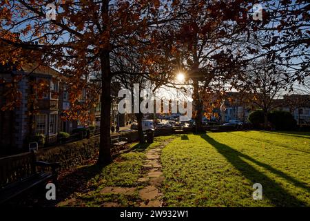 Das nachmittags-Wintersonnenlicht zieht durch Bäume mit Herbstlaub in Skipton Churchyard, Skipton, Nord-Yorkshire. Stockfoto