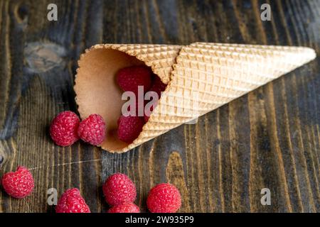 Rote reife Himbeeren mit Waffelbechern auf einem schwarzen Tisch, köstliche Himbeeren in einer Eisbecher Stockfoto