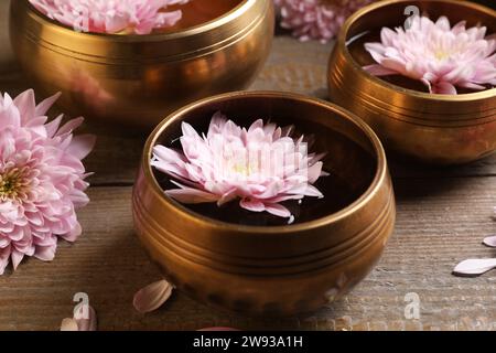 Tibetische Klangschalen mit Wasser und schönen Blumen auf Holztisch, Nahaufnahme Stockfoto