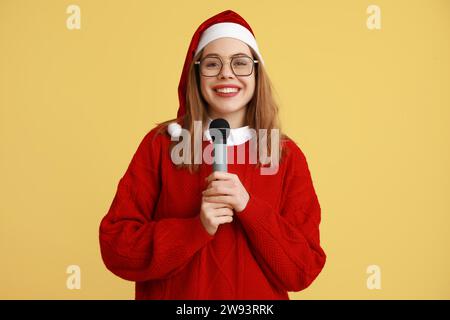 Junge Journalistin mit Weihnachtsmütze auf gelbem Hintergrund Stockfoto