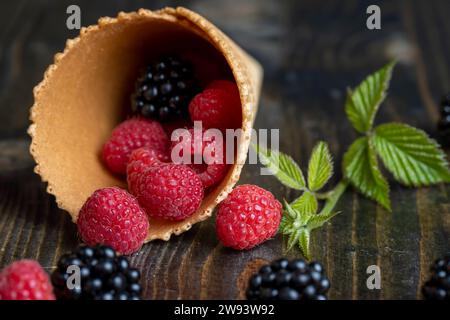 Rote reife Himbeeren mit Waffelbechern auf einem schwarzen Tisch, köstliche Himbeeren in einer Eisbecher Stockfoto