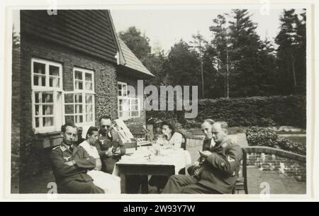 Deutsche Luftwaffe Soldaten draußen am Tisch, 1940 - 1941 Foto deutsche Luftwaffe Soldaten, eine Krankenschwester und eine Frau sitzen draußen an einem Tisch vor einem Haus, wahrscheinlich ein Ort zum Genesen. Im Hintergrund Kiefern. Niederlande fotografische Unterstützung Gelatine Silberdruck Besetzung  Krieg. Erholung  der Soldat aus dem Dienst. Ärztliche Hilfe und Pflege kranker und verwundeter Niederlande Stockfoto