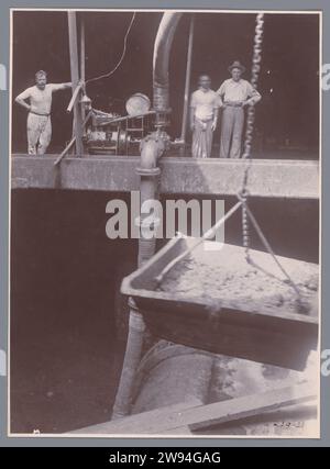 Entladung von Erts aus dem geräumigen IV, Anonym, 1921 Foto Entladung von Erz aus dem Frachtraum eines Schiffes. Eine Pumpe wird von einem höheren Deck aus von einem Holländer aus betrieben, neben ihm zwei weitere Männer, September 1921. Nicht Nummeriert. Teil der Gruppe von Einzelfotos über den Bau des Hafens Belawan an der Küste für Medan, Sumatra 1921-1922. Belawan Fotomaterial Steamsailer. Crew  Schiff. Frachtschiff Belawan Stockfoto