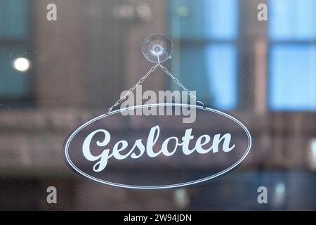 Schwarzes Schild, das an der Glastür eines Ladens hängt und auf Niederländisch steht: 'Gesloten', was im Englischen 'geschlossen' bedeutet. Stockfoto