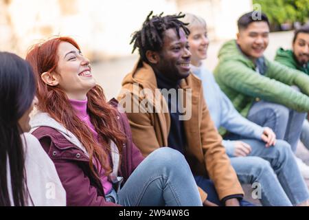 Lachende rothaarige Frau mit verschiedenen Freunden, die ein zwangloses Treffen im Freien genießt, verkörpert die Freude der Gemeinschaft. Stockfoto