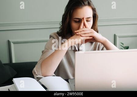 Gestresst und überarbeitet Junge Frau mit Laptop, die Müdigkeit, Druck, Migräne und Stress bekämpfen kann. Moderne Herausforderungen Am Arbeitsplatz. Traurige Frau, die an OV leidet Stockfoto