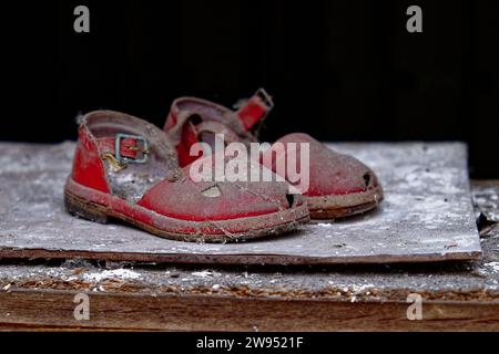 Zwei abgenutzte rote Sandalen mit Schnallen, die auf einer staubigen und schmutzigen Oberfläche liegen. Stockfoto