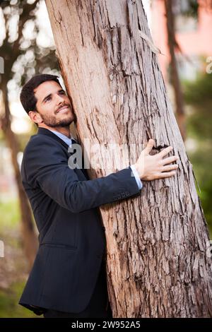 Ein Geschäftsmann umarmt einen Baumstamm Stockfoto