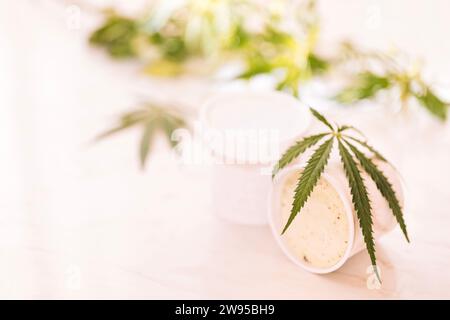 Ein Hanfblatt liegt auf einem nachgeahmten Glas Eis auf einem weißen Marmortisch. Grüne Cannabisblätter auf dem Hintergrund. Bio-Lebensmittel und Gesundheit. Stockfoto