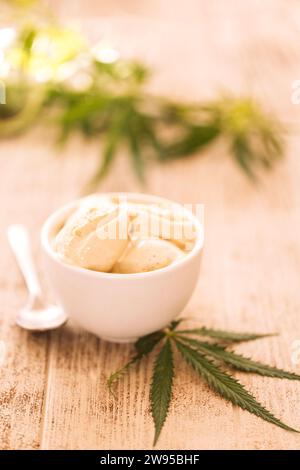 Ein Hanfblatt liegt auf einem nachgeahmten Glas Eis auf einem Holztisch. Grüne Cannabisblätter auf dem Hintergrund. Bio-Lebensmittel und Gesundheit. Stockfoto