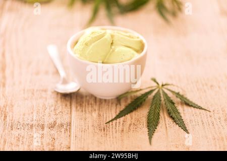 Ein Hanfblatt liegt auf einem nachgeahmten Glas Eis auf einem Holztisch. Grüne Cannabisblätter auf dem Hintergrund. Bio-Lebensmittel und Gesundheit. Stockfoto