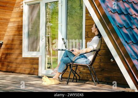 Digitaler Nomade mit Laptop auf der Veranda eines kleinen Blockhauses Stockfoto