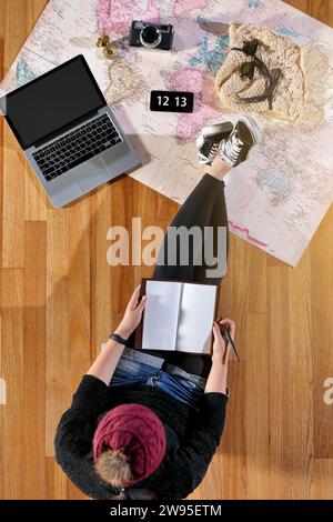 Eine Frau, die auf einer Karte sitzt und sich mit Reiseaccessoires auf eine Reise vorbereitet Stockfoto