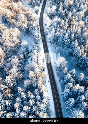 Kurvenreiche Straße führt durch verschneiten Wald zu Beginn des Sonnenaufgangs, aus der Vogelperspektive, Schwarzwald Dobel, Deutschland Stockfoto