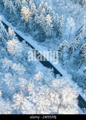 Eine Luftaufnahme zeigt eine Straße, die sich durch einen schneebedeckten Wald, Gechingen, Luftaufnahme, Schwarzwald, Deutschland Stockfoto