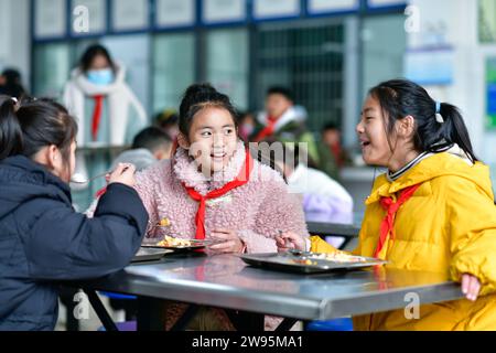 (231224) -- ANSHUN, 24. Dezember 2023 (Xinhua) -- Ji Xue (C) hat kostenloses Mittagessen in der Schule im Bezirk Xixiu der Stadt Anshun, südwestchinesische Provinz Guizhou, 22. Dezember 2023. Vor fünf Jahren begannen die sechsjährige Ji Xue und ihre Familie aus der ethnischen Gruppe der Miao ein neues Leben. Dank der Bemühungen zur Armutsbekämpfung wurden sie in ein neues Zuhause aus unwirtlichen Bergregionen und abgelegenen Gebieten umgesiedelt. In den letzten fünf Jahren sind die Unterstützungseinrichtungen in der Umsiedlungsgemeinschaft, in der Ji heute lebt, immer besser geworden. Früher dauerte es mehr als zwei Stunden, bis Ji zur Schule auf einer Bergstraße kam Stockfoto