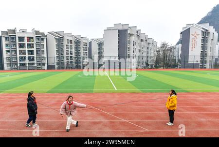 (231224) -- ANSHUN, 24. Dezember 2023 (Xinhua) -- Ji Xue (C) spielt mit Klassenkameraden in der Schule, mit ihren umgewanderten Häusern im Bezirk Xixiu der Stadt Anshun, südwestchinesische Provinz Guizhou, 22. Dezember 2023. Vor fünf Jahren begannen die sechsjährige Ji Xue und ihre Familie aus der ethnischen Gruppe der Miao ein neues Leben. Dank der Bemühungen zur Armutsbekämpfung wurden sie in ein neues Zuhause aus unwirtlichen Bergregionen und abgelegenen Gebieten umgesiedelt. In den letzten fünf Jahren sind die Unterstützungseinrichtungen in der Umsiedlungsgemeinschaft, in der Ji heute lebt, immer besser geworden. Früher dauerte Ji mehr als zwei Stunden Stockfoto